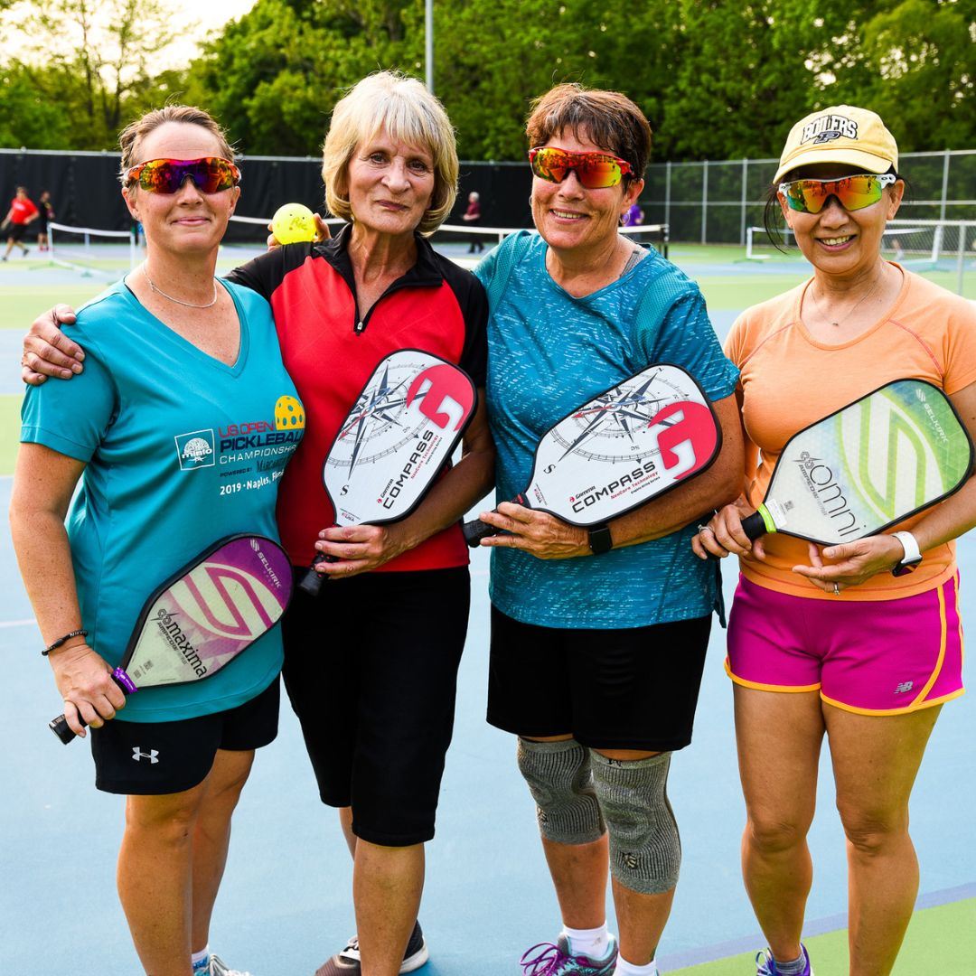 A group of four women on the pickleball court with their paddles