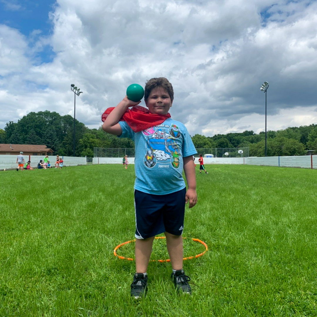 Young kid holding up a dodgeball in a grassy field