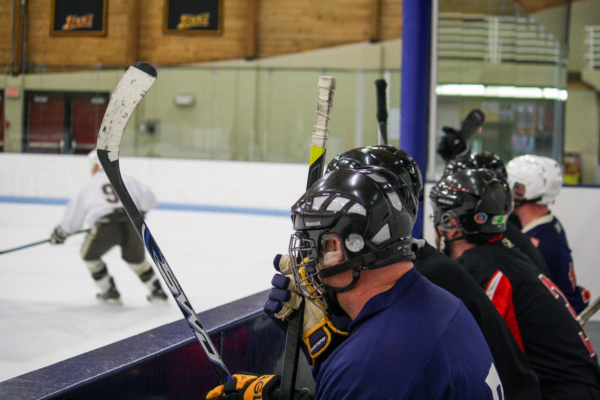 A group of adult hockey league teammates behind the boards watching the game