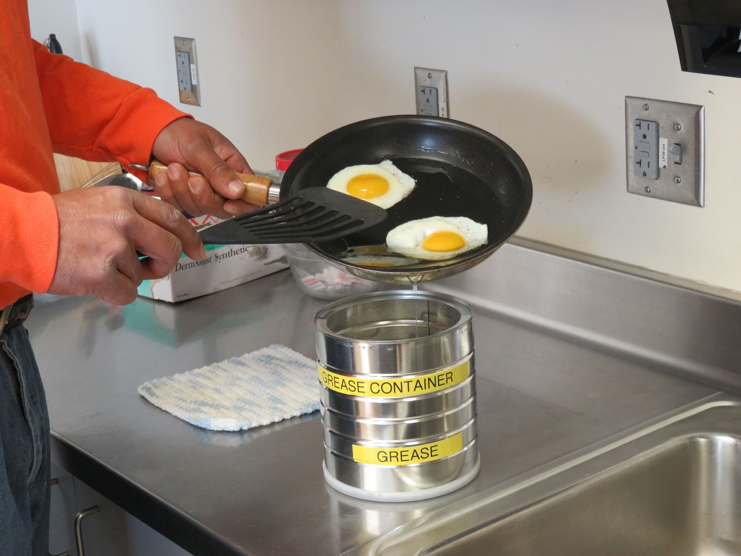 Person putting grease from frying eggs into a coffee can-sized collection container.