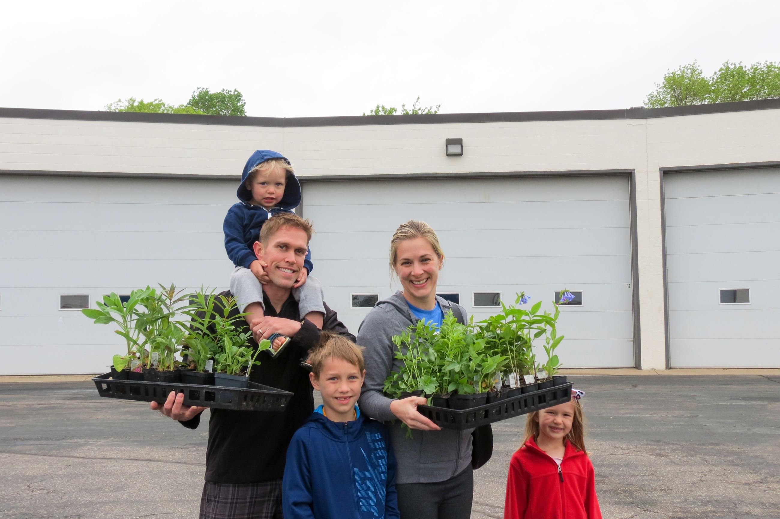 Two parents holding plant seedlings with three kids